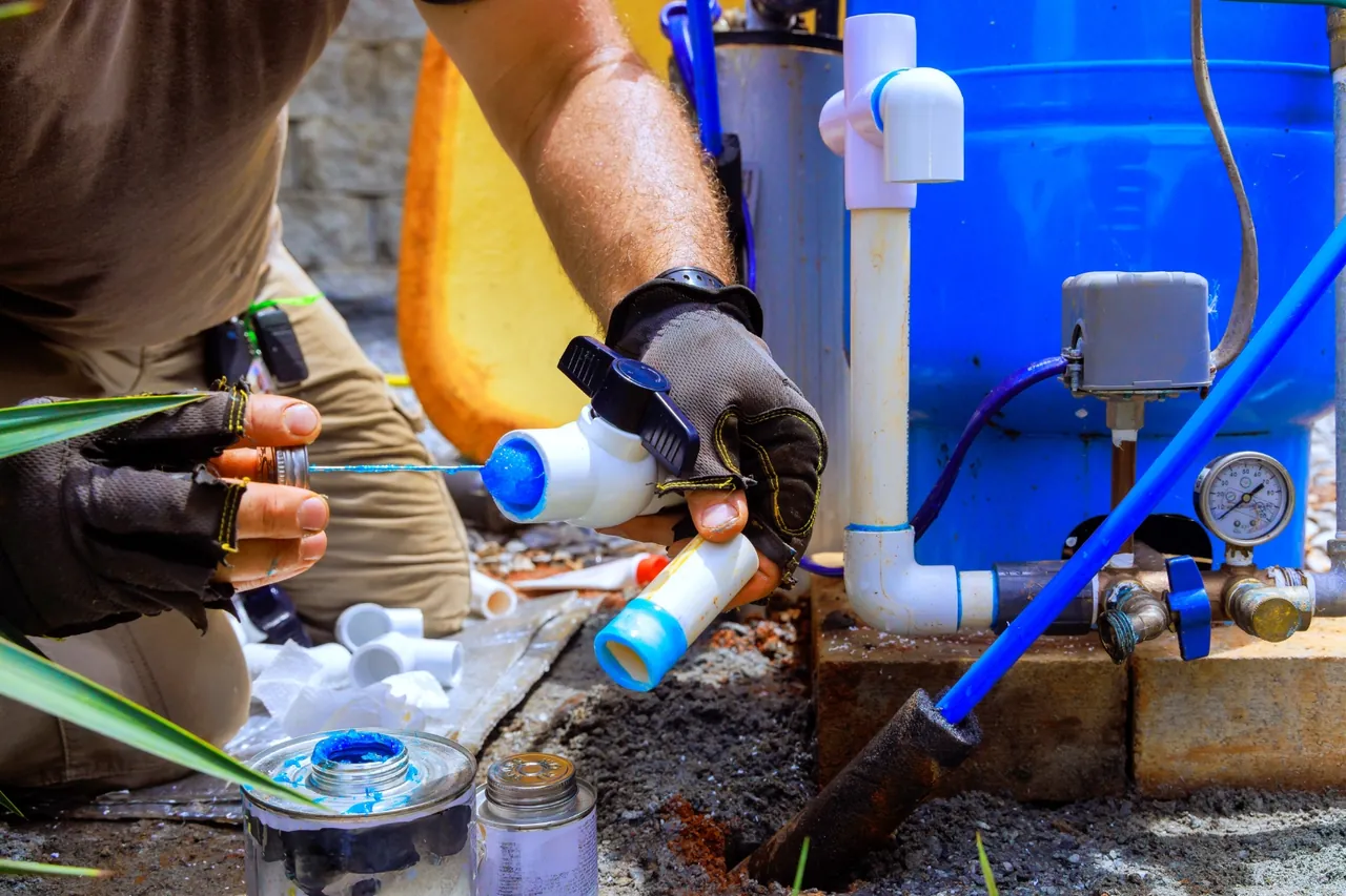 Técnico de luvas montando conexões de PVC ao lado do reservatório azul, parte da instalação residencial