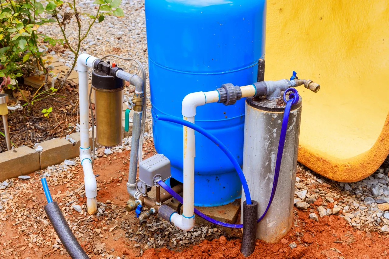 Sistema de pressurização de poço instalado em quintal, com tanque azul, filtro e tubulação